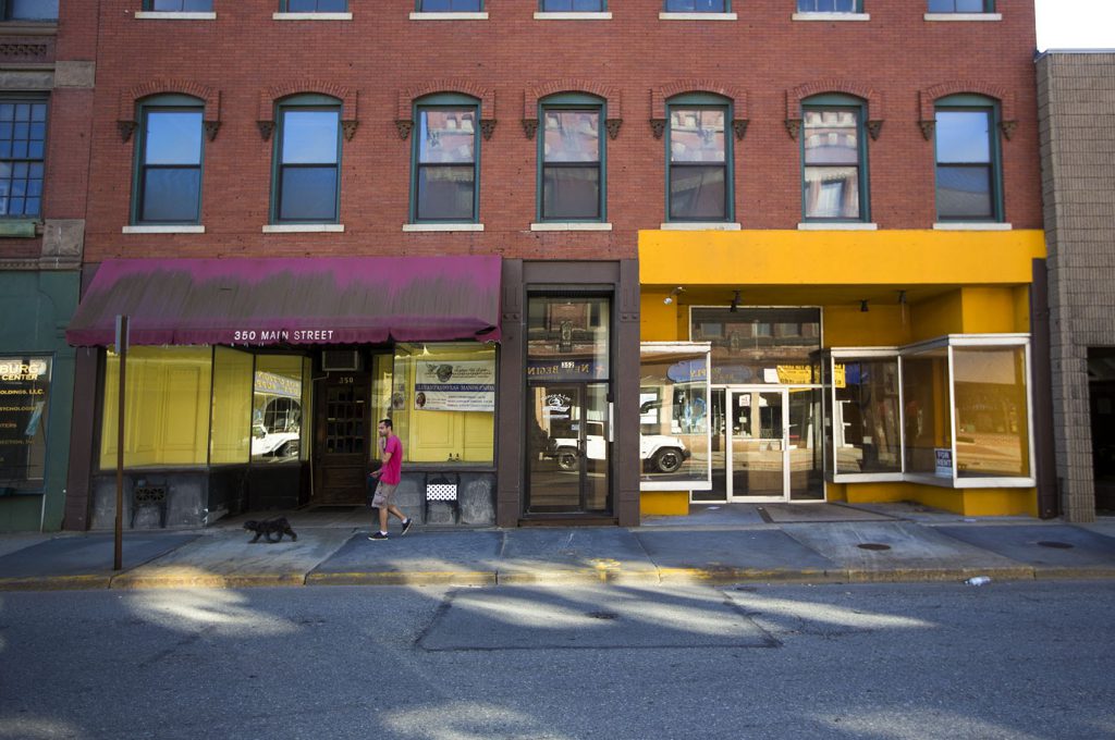 A man walks his dog in front of vacant commercial spaces along Main Street in Fitchburg. (Credit: Jesse Costa/WBUR)