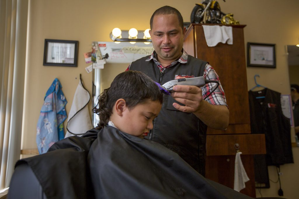 Luis Feliciano cuts the hair of a young boy at the newly opened Brothers Barber Shop on Main Street in Fitchburg. (Credit: Jesse Costa/WBUR)