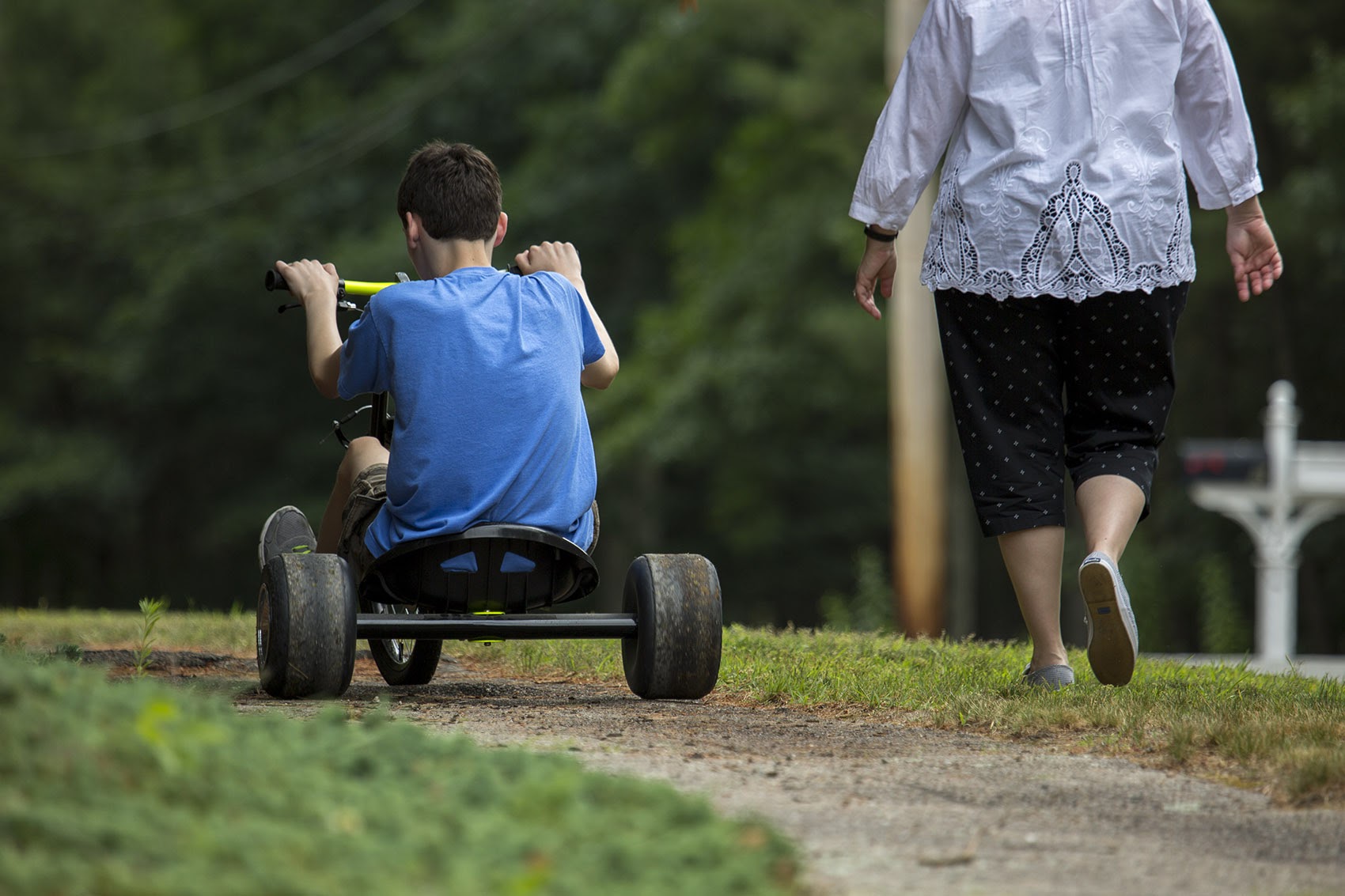 Marie walks with her 13-year-old son, who has been diagnosed on the autism spectrum, as he rides his bike through their Norfolk neighborhood during the first weeks of summer vacation. (Jesse Costa/WBUR)