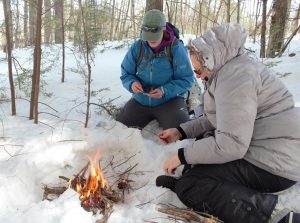 Julia Wilcox and Claire Rouge tend to a fire they made during BOW's winter survival skills class. Photo by Annie Ropeik for NHPR