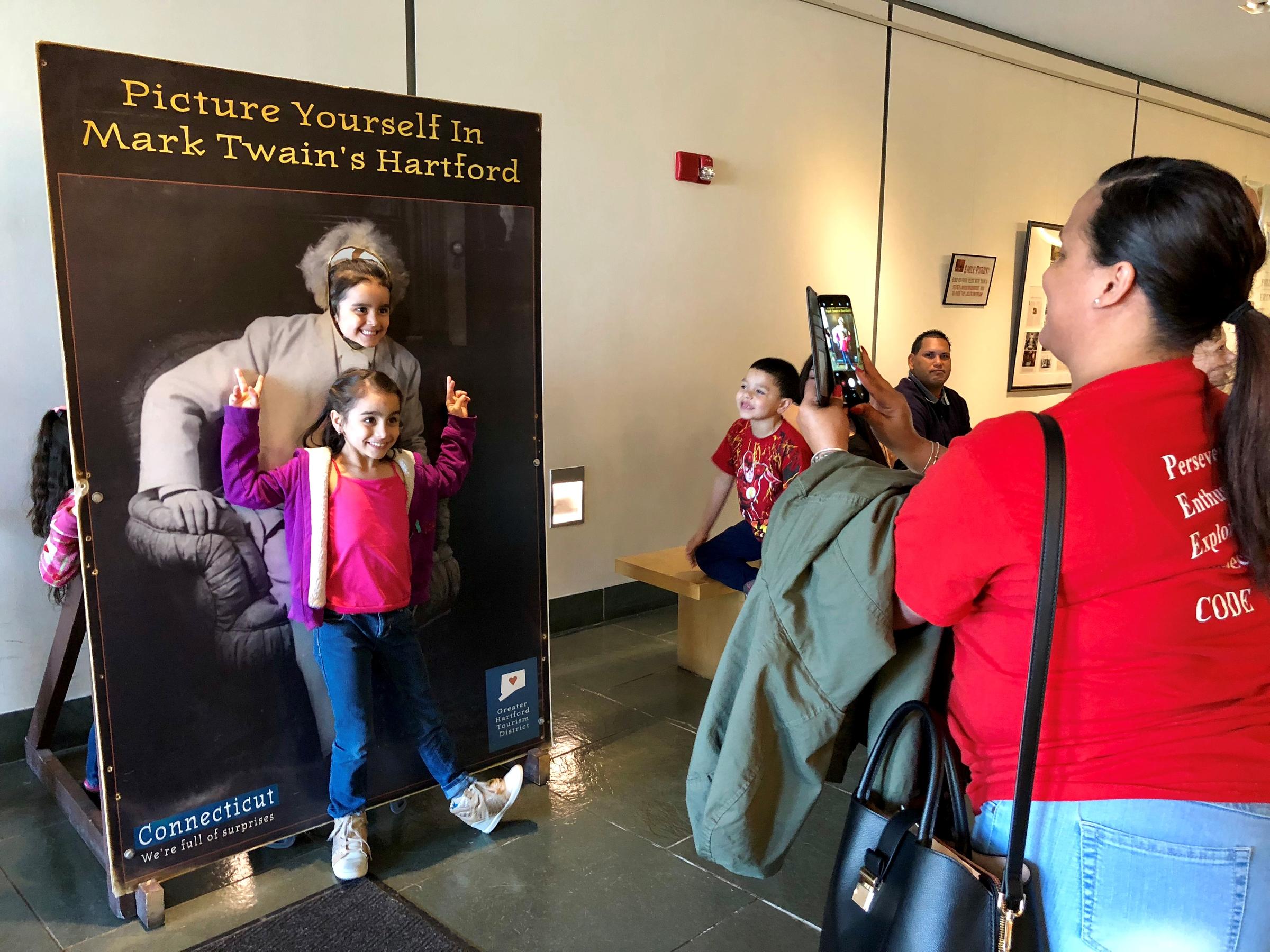 Sanchez School employee Sally Vazquez, right, takes a photo of Hartford students in the lobby of the Mark Twain House & Museum. Families displaced from Puerto Rico were invited to the American landmark. Photo by Vanessa de la Torre for Connecticut Public Radio