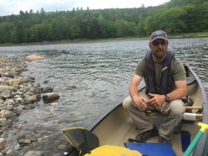 Greg Caruso, ferryman for the Appalachian Trail. In season, he takes through-hikers across the Kennebec River, a few miles downstream from where CMP wants to build a major transmission line. He opposes the plan – even with CMP’s offer to donate land and money in compensation. Photo by Fred Bever for Maine Public