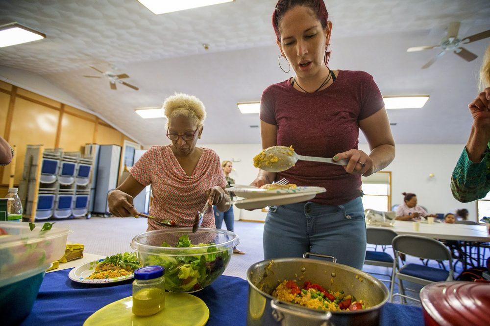 Genie Garda, a la derecha, y Amada Gregory toman alimentos en la comida improvisada en Dracut. Gregory es un abogado de familia en la Alianza de Lowell. Garda se reubicó desde Puerto Rico luego de María. (Jesse Costa/WBUR)