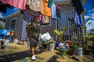 Angelina Arroyo sprays her driveway down during a hot afternoon in Punta Santiago. Her husband had a heart attack shortly after the hurricane last year and passed away soon after. Photo by Jesse Costa for WBUR