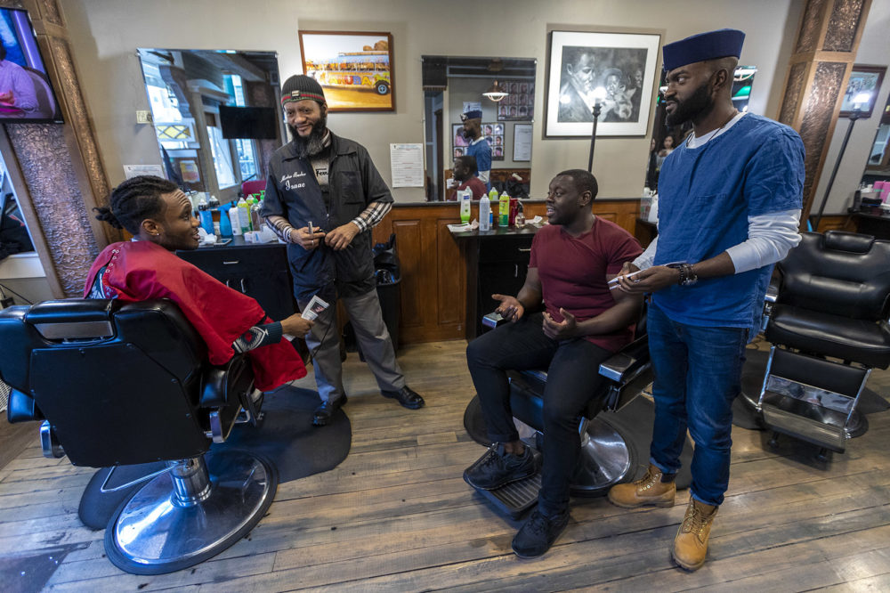 From right to left: Bright Genty and his father, master barber Isaac, speak with "Barber Shop Chronicles" actor Ekow Quartey and the production's writer Inua Ellams at Headlines Unisex Barbershop in Cambridge. Photo by Jesse Costa for WBUR