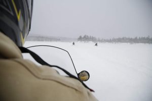 Snowmobilers cross a frozen lake. Photo by Nick Woodward for Maine Public