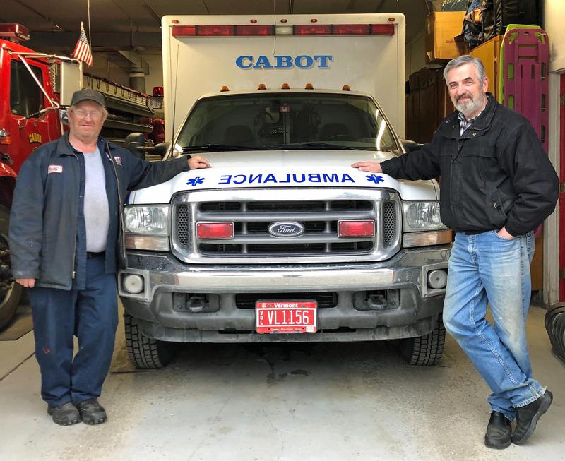 EMT Andy Luce, left, and Cabot Select Board Chair Michael Hogan, right, stand with the town ambulance, housed at the Cabot Fire Department. The town's emergency ambulance service will stop transporting patients in June. Photo by Amy Kolb Noyes for VPR