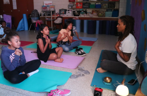 As part of the Come and Learn Mindfulness program at Curiale School in Bridgeport, yoga instructor Shinda DeRosa sits cross-legged with her students, encouraging them to place their hands over their hearts and meditate about their loved ones. Photo by Christian Carter for WSHU.