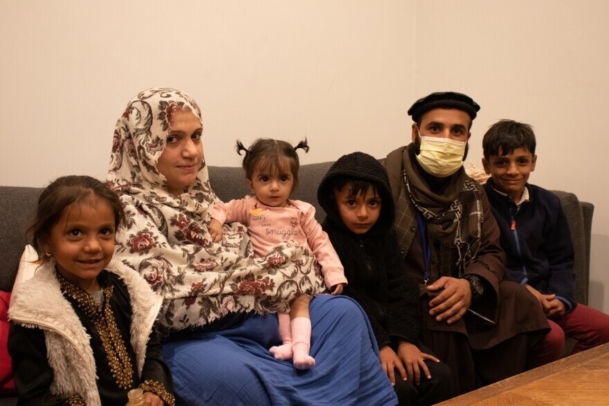 An Afghan family with two adults and three children sit on a couch after recently resettling in Massachusetts with help of the International Institute of New England.