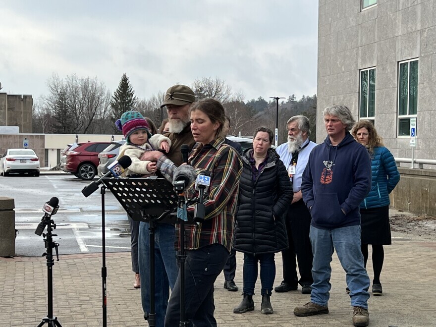 Adrienne Lee of New Beat Farm, an organic operation in Knox, addresses reporters at a press conference at the Maine State House on PFAS legislation on Wednesday as Ken Lamson and their toddler daughter watch.