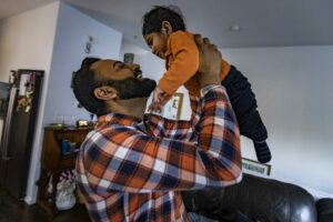 Raj Paik lifts his nine-month-old son Siraj after getting home from work.