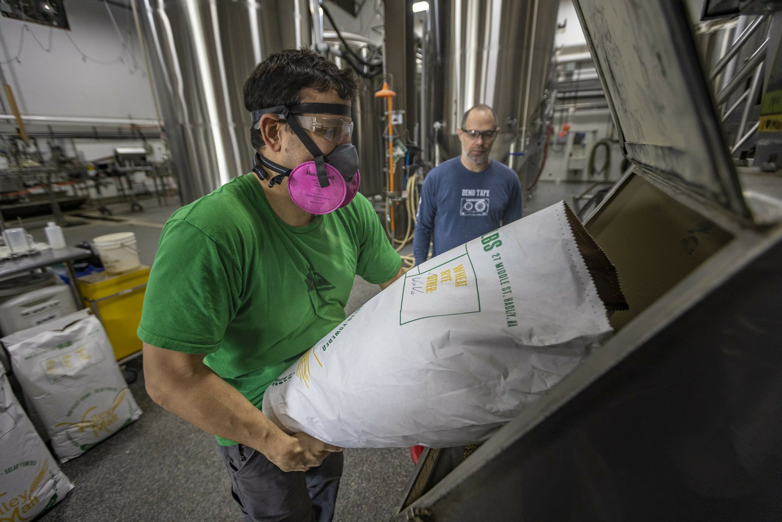 Matthew Steinberg watches as Joe Forte pours Wart Hog Wheat from Oechsner Farm in New York and malted by Valley Grain Milling in Hadley, Massachusetts into a mill at Exhibit 'A' Brewing to be used to brew one of their flagship beers, Cat’s Meow IPA. 