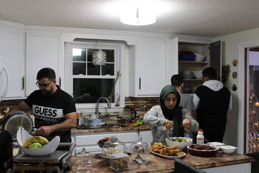 Mashan Manahe, left, transfers a meat dish from the stove while his wife, Zainab, makes a salad and their two sons, Omar and Nasir, get plates out of the cabinet. The Manahe family enjoys a variety of specialty food during Ramadan, including dates, sambousas, and sweets. 