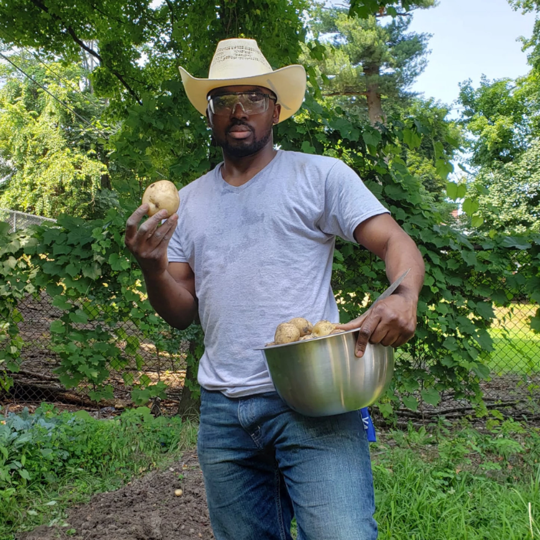Hameed Bello, wearing a cowboy hat, holds a bowl of potatoes on his farm, Agric Organics in Wilbraham, Massachusetts.