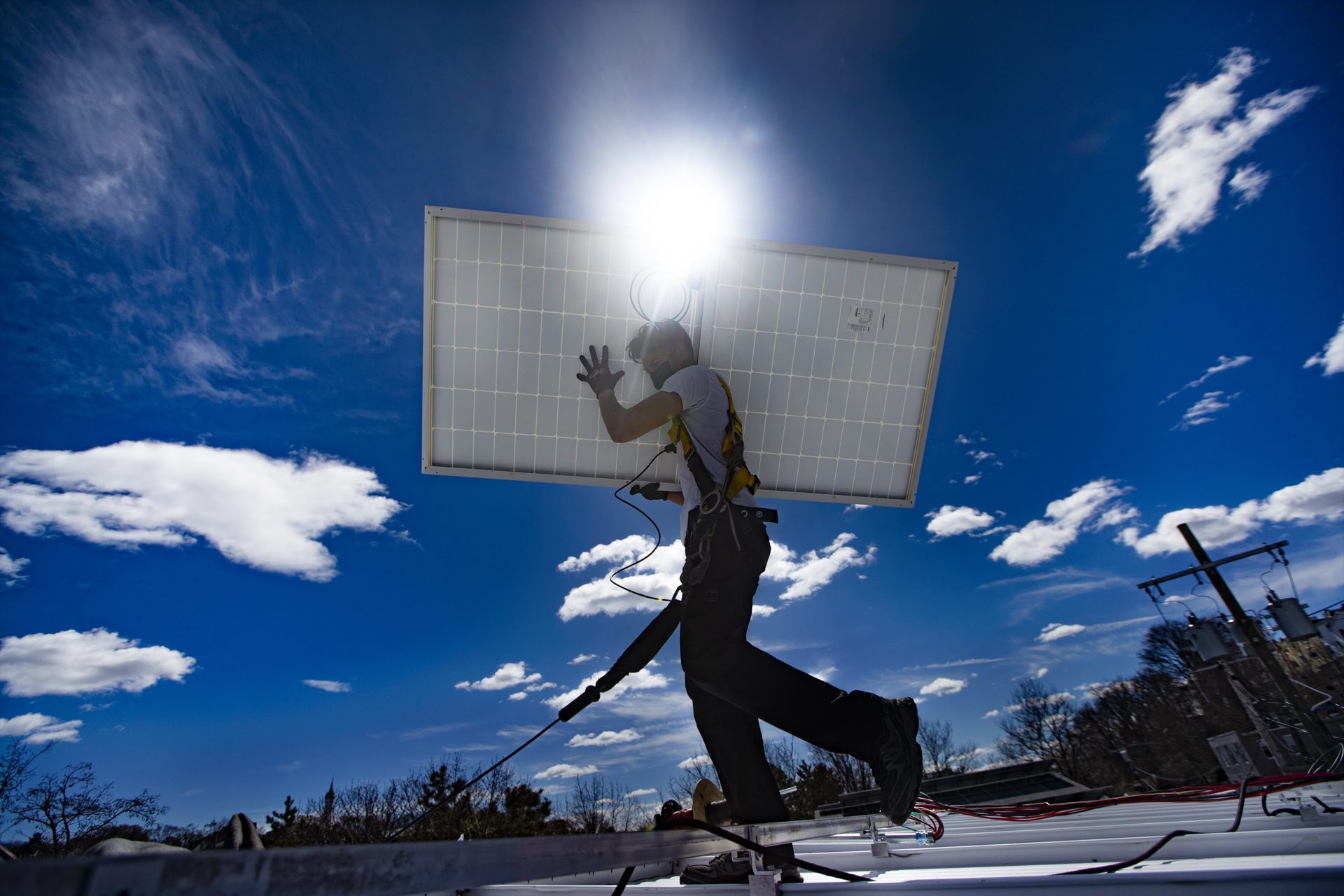 A technician walks with a solar panel across the rooftop during a solar panel installation at Boston Building Resources in Jamaica Plain. 