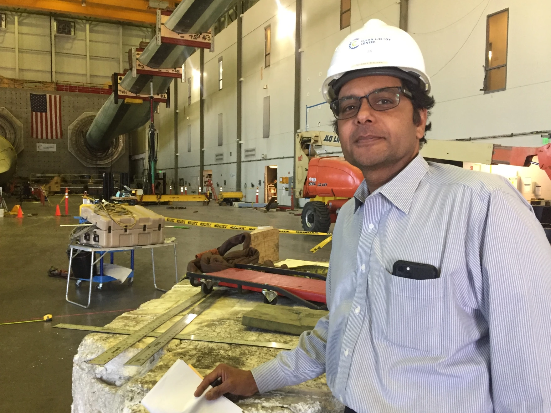 WTTC Executive Director Rahul Yarala is standing with a white hard hat in front of a turbine blade. 