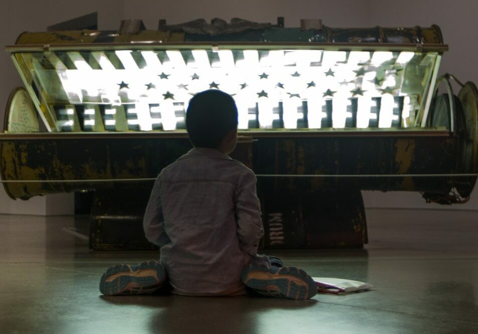 Nine-year-old Danny Zheng colors on the floor in front of Nari Ward's "Tanning Bed." Photo by Jesse Costa for WBUR.